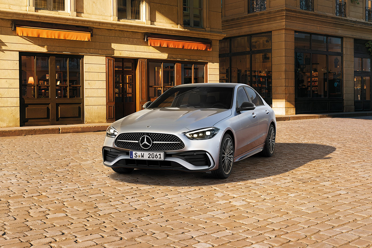 Auf dem Bild steht ein silberfarbenes Fahrzeug der Marke Mercedes‑Benz auf einer gepflasterten Fläche. Das Auto ist schräg von vorne zu sehen, wodurch sowohl die Front als auch die linke Seite sichtbar sind. Das Fahrzeug besitzt einen markanten Kühlergrill mit dem Mercedes‑Benz‑Logo in der Mitte, LED‑Scheinwerfer und mehrspeichige Leichtmetallräder.