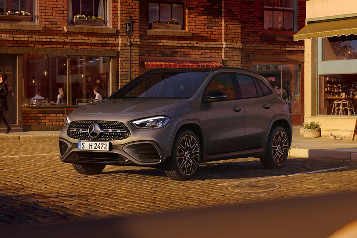 Auf dem Bild steht ein graues SUV‑Fahrzeug der Marke Mercedes‑Benz auf einer gepflasterten Straße. Das Auto ist schräg von vorne zu sehen, sodass die Fahrzeugfront und die linke Seite sichtbar sind. Das Fahrzeug besitzt große Leichtmetallräder, markante LED‑Scheinwerfer und einen Kühlergrill mit dem Mercedes‑Benz‑Logo in der Mitte.