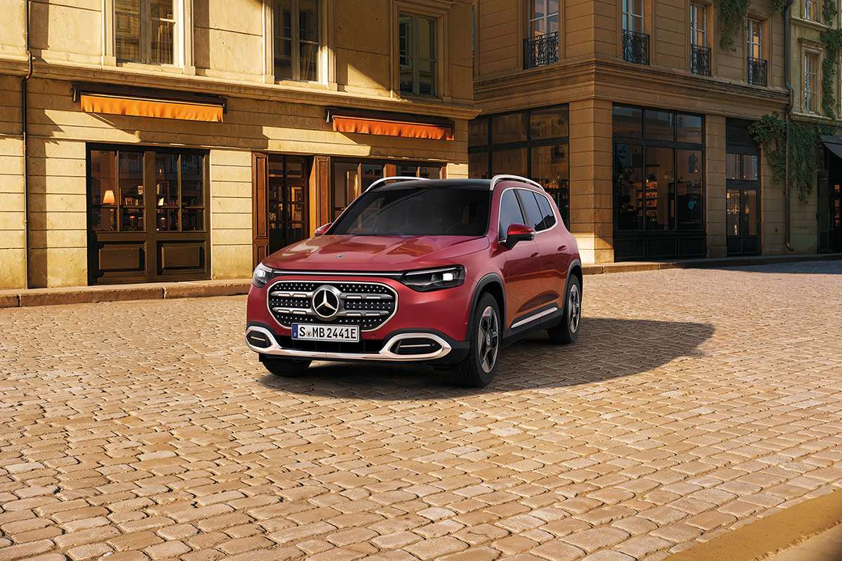 Auf dem Bild ist ein rotes SUV‑Fahrzeug der Marke Mercedes‑Benz zu sehen. Das Fahrzeug steht auf einer hellen, gepflasterten Straße aus gleichmäßigen Natursteinquadern. Der SUV ist frontal leicht zur linken Seite gedreht. Zu erkennen sind ein großer Kühlergrill mit dem Markenlogo, LED‑Scheinwerfer und schwarze Scheiben.