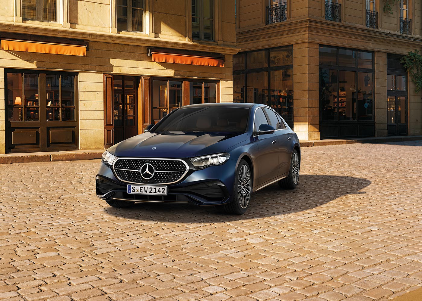 Auf dem Bild steht ein dunkelblaues Fahrzeug der Marke Mercedes‑Benz auf einer gepflasterten Fläche. Das Auto ist schräg von vorne zu sehen, sodass die Front und die linke Fahrzeugseite sichtbar sind. Es verfügt über einen geschlossenen Kühlergrill mit dem Mercedes‑Benz‑Logo in der Mitte, schmale LED‑Scheinwerfer und mehrspeichige Leichtmetallräder.