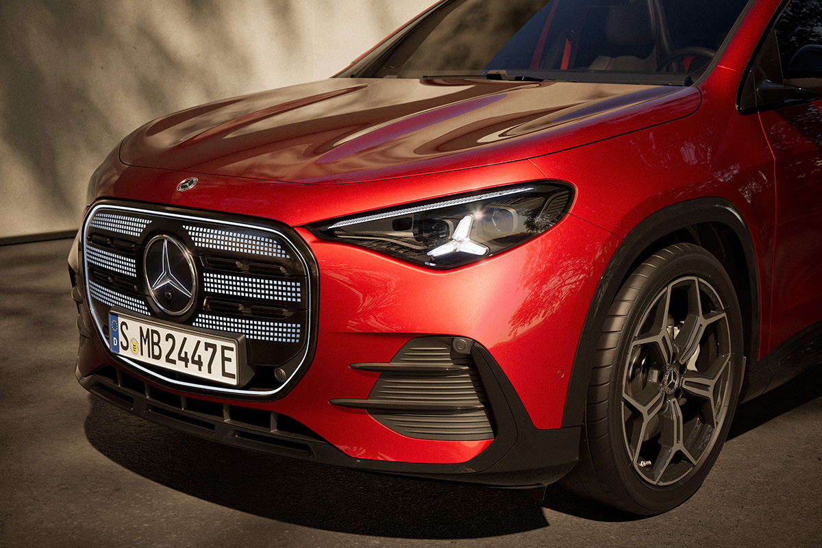 Nahaufnahme der Front eines roten Mercedes Elektro SUV mit beleuchtetem Kuehlergrill modernem Scheinwerfer und Vorderrad auf einer Strasse bei Tageslicht.