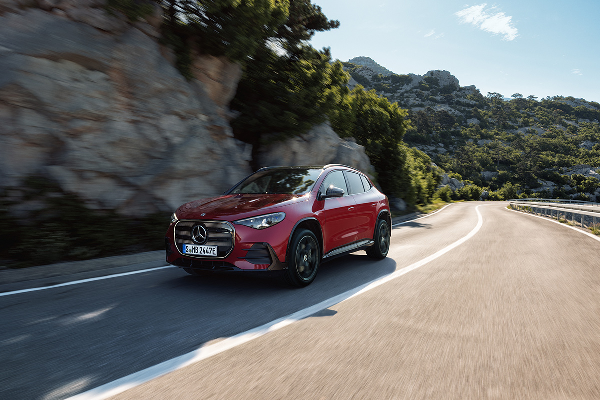 Roter Mercedes Elektro SUV faehrt auf einer kurvigen Strasse durch eine bergige Landschaft mit Felsen und Vegetation bei Tageslicht.
