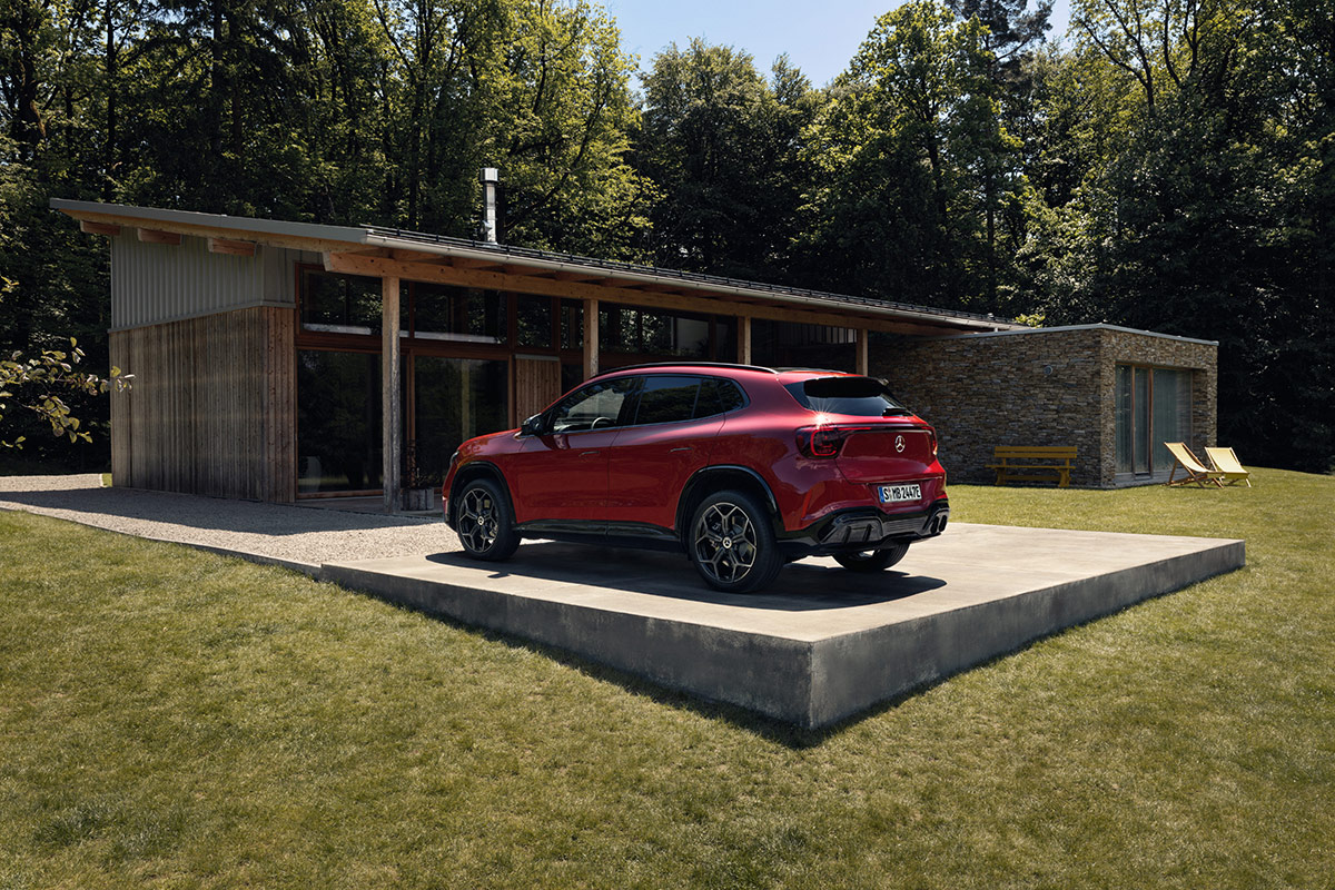 Roter Mercedes SUV steht auf einer Betonflaeche vor einem modernen Wohnhaus mit grosser Fensterfront in naturnaher Umgebung mit Baeumen und Rasenflaeche.