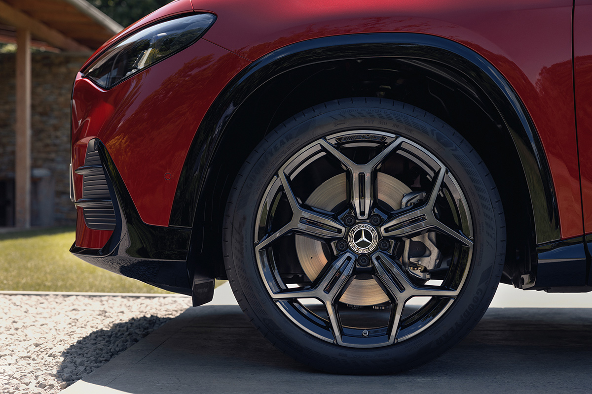 Detailansicht des Vorderrads eines roten Mercedes SUV mit Leichtmetallfelge Reifen und sichtbarer Bremsanlage auf befestigter Flaeche vor einem Wohngebaeude.