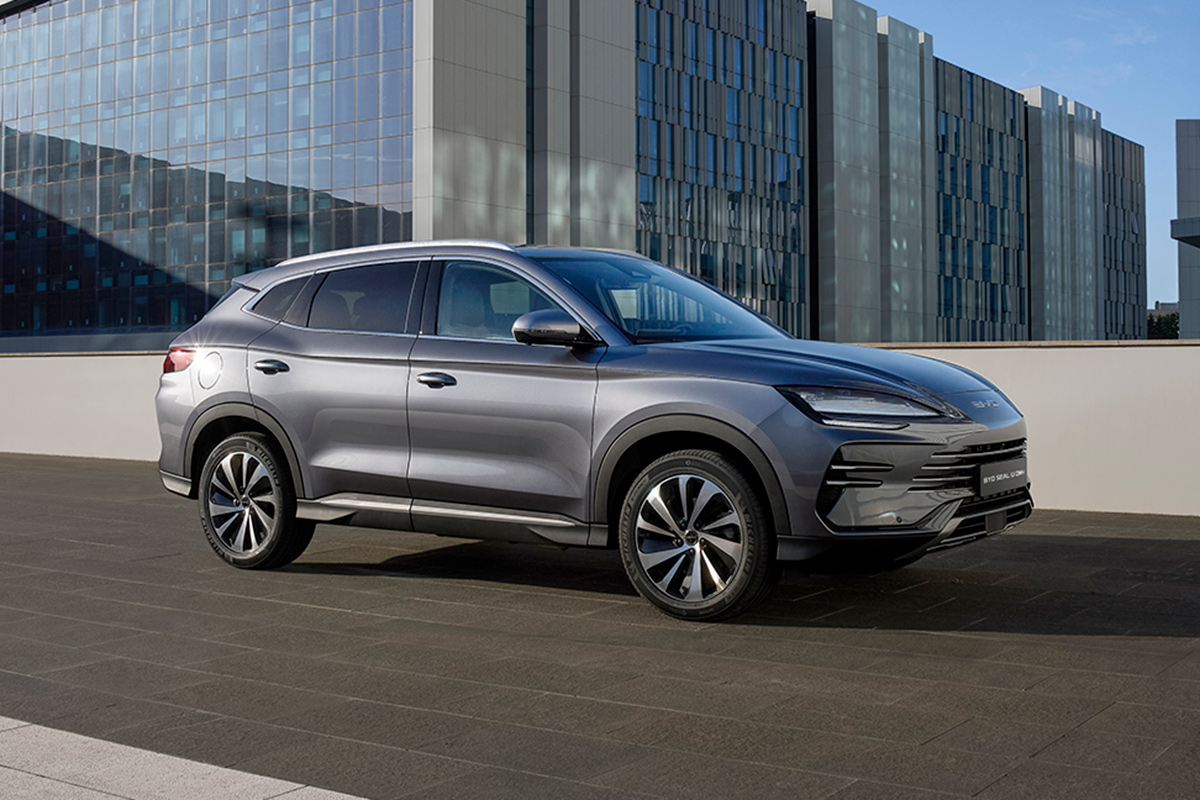 Graues SUV steht auf einer Dachterrasse vor modernen Glasgebaeuden bei Tageslicht Seitenansicht mit klaren Linien grossen Raedern und getoenten Scheiben urbanes Umfeld ohne Personen