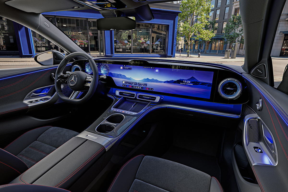 Innenansicht des Cockpits einer Mercedes Benz C Klasse mit digitalem Hyperscreen und blauer Ambientebeleuchtung. Das schwarze Interieur zeigt sportliche Sitze mit roten Ziernaehten und ein Lenkrad.