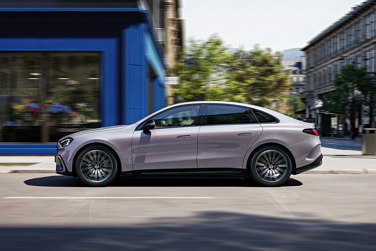 Seitenansicht einer silbergrauen Mercedes Benz C Klasse Limousine bei der Fahrt durch eine Stadt. Das Fahrzeug besticht durch seine fliessende Linienfuehrung und grosse dunkle Mehrspeichenfelgen.