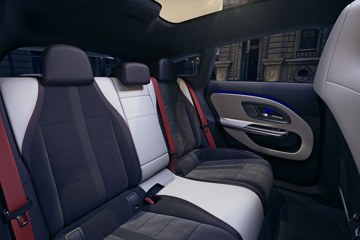 Ruecksitzbereich eines Autos mit zweifarbigem Polster in Schwarz und Weiss, roten Gurten und moderner Tuereverkleidung. Oben ist ein grosses Glasdach sichtbar, draussen eine stadtliche Szene.