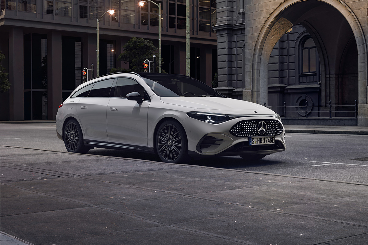 Weisses Kombifahrzeug steht in einer stadtlichen Umgebung. Sichtbar sind schlanke LED‑Scheinwerfer, schwarzes Panorama­dach, markante Felgen und die elegante, dynamische Seitenlinie.