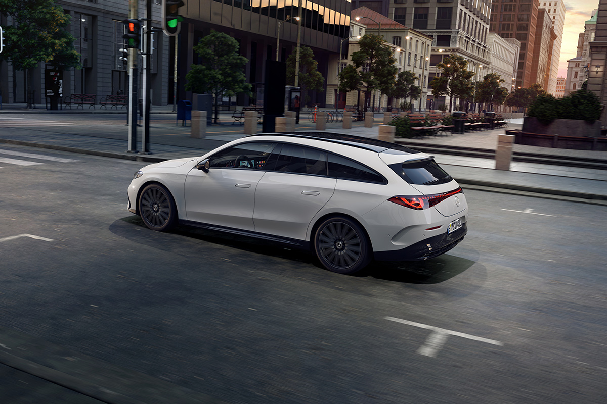 Weisses Kombifahrzeug faehrt durch eine stadtliche Umgebung. Sichtbar sind das schwarze Panoramadach, schmale LED‑Rueckleuchten, schwarze Felgen und die elegante, dynamische Seitenlinie.