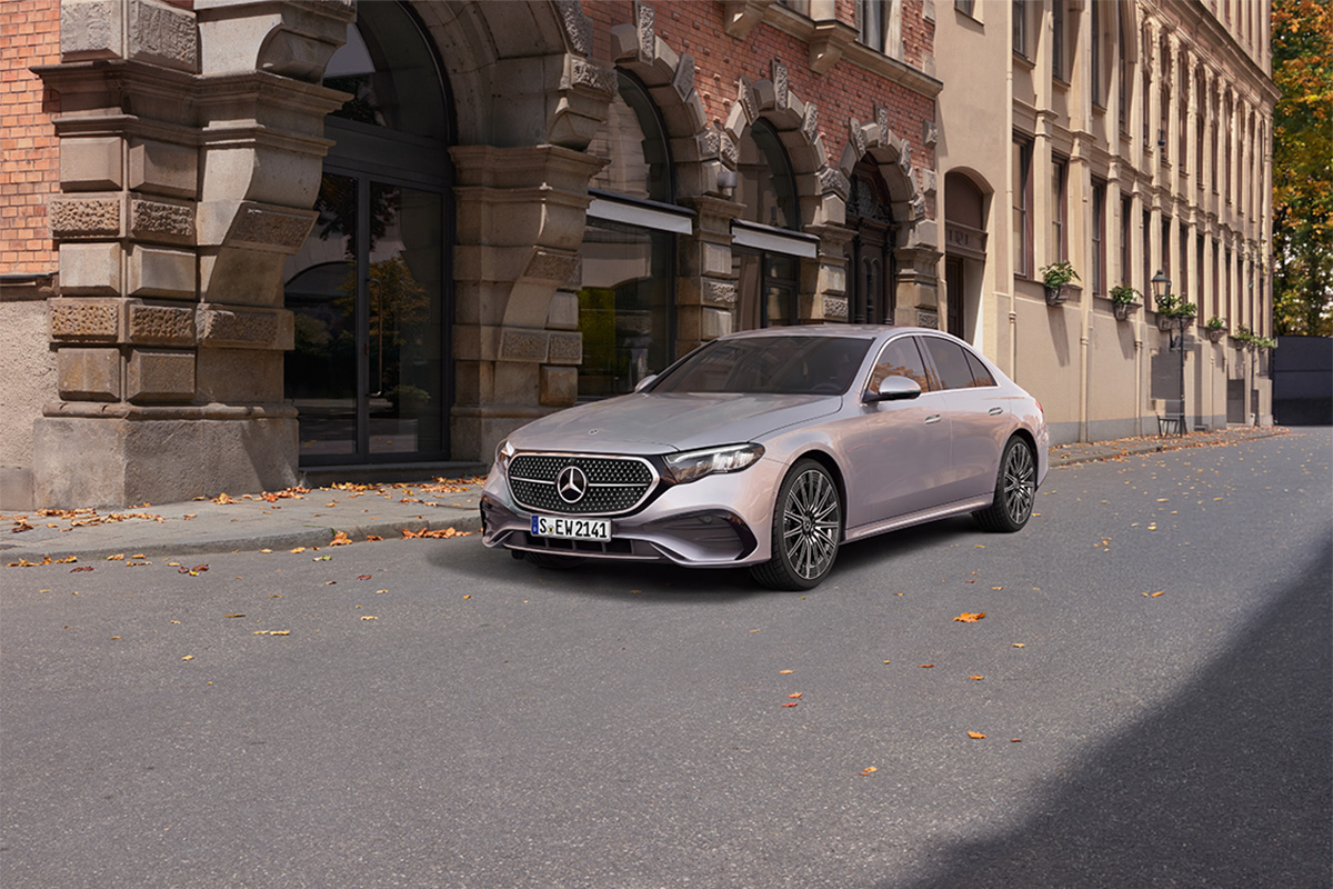 Silberne Mercedes-Benz E-Klasse Limousine steht auf einer ruhigen Strasse vor einem historischen Gebaeude mit Rundboegen. Herbstliche Blaetter liegen auf der Fahrbahn.