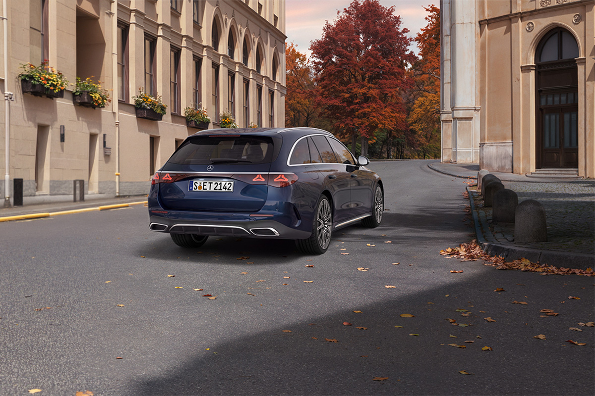 Blaues Mercedes-Benz E-Klasse T-Modell steht auf einer ruhigen Strasse zwischen historischen Gebaeuden. Im Hintergrund sind herbstlich gefaerbte Baeume und verstreute Blaetter zu sehen.