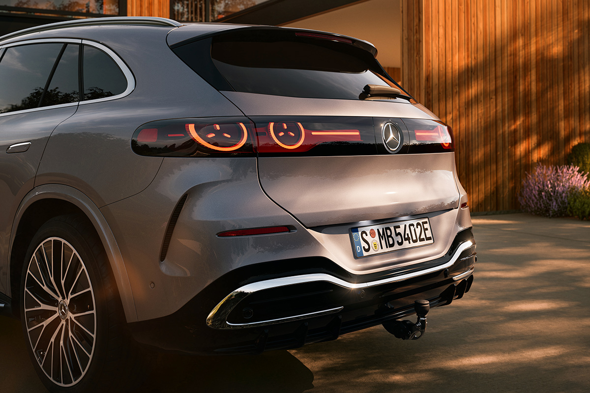 Heckansicht eines silbernen SUV in einer Einfahrt. Sichtbar sind LED‑Rueckleuchten mit animiertem Muster, schwarze Felgen, Chromdetails und eine ausgeklappte Anhängerkupplung.