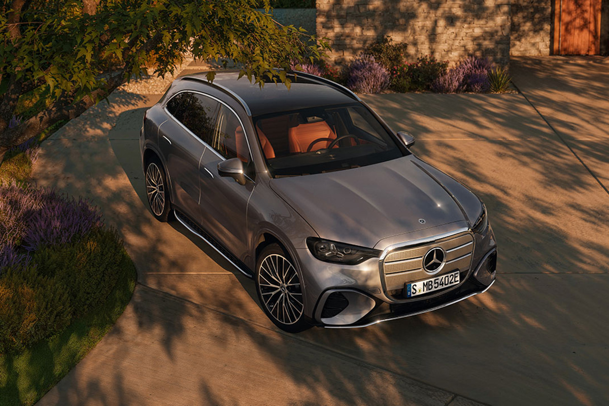 Vogelperspektive auf einen silbernen Mercedes-Benz GLC EV mit braunen Ledersitzen auf einer Einfahrt neben Lavendelstraeuchern. Das Fahrzeug steht im warmen Abendlicht vor einer Steinmauer
