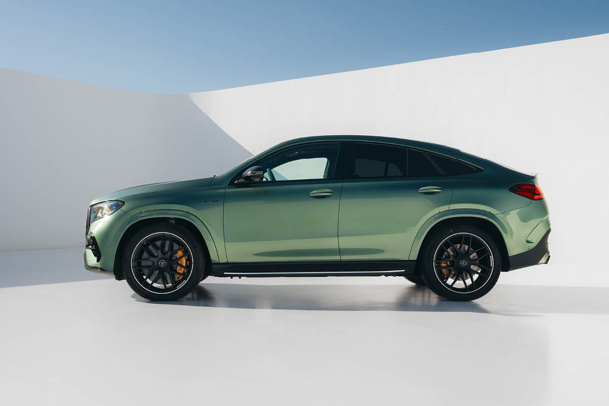 Das Bild zeigt das Fahrzeug in einer vollständigen Seitenansicht. Der Mercedes-Benz AMG GLE 63 S 4MATIC+ ist in einem matten Grünton gehalten und steht in einer minimalistischen Umgebung mit hellen Wänden und gleichmäßiger Beleuchtung. Die coupéartige Dachlinie verleiht dem SUV eine dynamische Silhouette. Große, schwarze Leichtmetallräder mit sichtbaren, gelb/orangefarbenen Bremssätteln betonen die sportliche Performance. Entlang der Seite verlaufen klare Linien sowie ein Trittbrett unterhalb der Türen, das den Einstieg erleichtert. Die Fenster sind leicht abgedunkelt, und die gesamte Fahrzeugform wirkt kraftvoll, elegant und aerodynamisch zugleich.