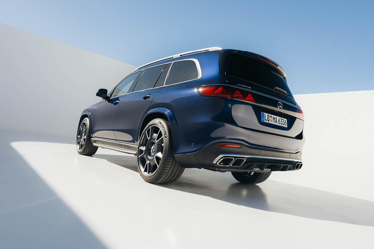 Das Bild zeigt den Mercedes-Benz AMG GLE 63 S 4MATIC+ in einer modernen, minimalistischen Umgebung. Das Fahrzeug ist in einem dunklen Blauton lackiert und von hinten leicht schräg dargestellt, wodurch die sportliche Linienführung gut zur Geltung kommt. Die schmalen LED-Rückleuchten sind aktiviert und bilden ein markantes Lichtdesign. Am Heck sind vier Auspuffendrohre sichtbar, eingefasst in einen sportlichen Diffusor. Große, mehrspeichige Leichtmetallfelgen unterstreichen die leistungsorientierte Ausrichtung des SUV. Die Umgebung besteht aus glatten, hellen Flächen mit starken Licht- und Schattenkontrasten.