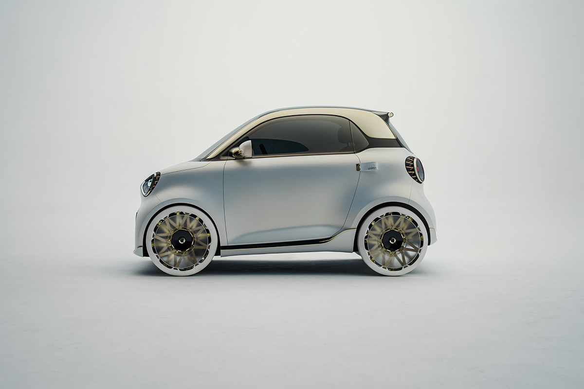 Seitenansicht eines kompakten weissen Smart Concept Elektroautos mit goldfarbenen Akzenten an Dach und Felgen vor neutralem hellem Hintergrund. Das Design ist minimalistisch und futuristisch.
