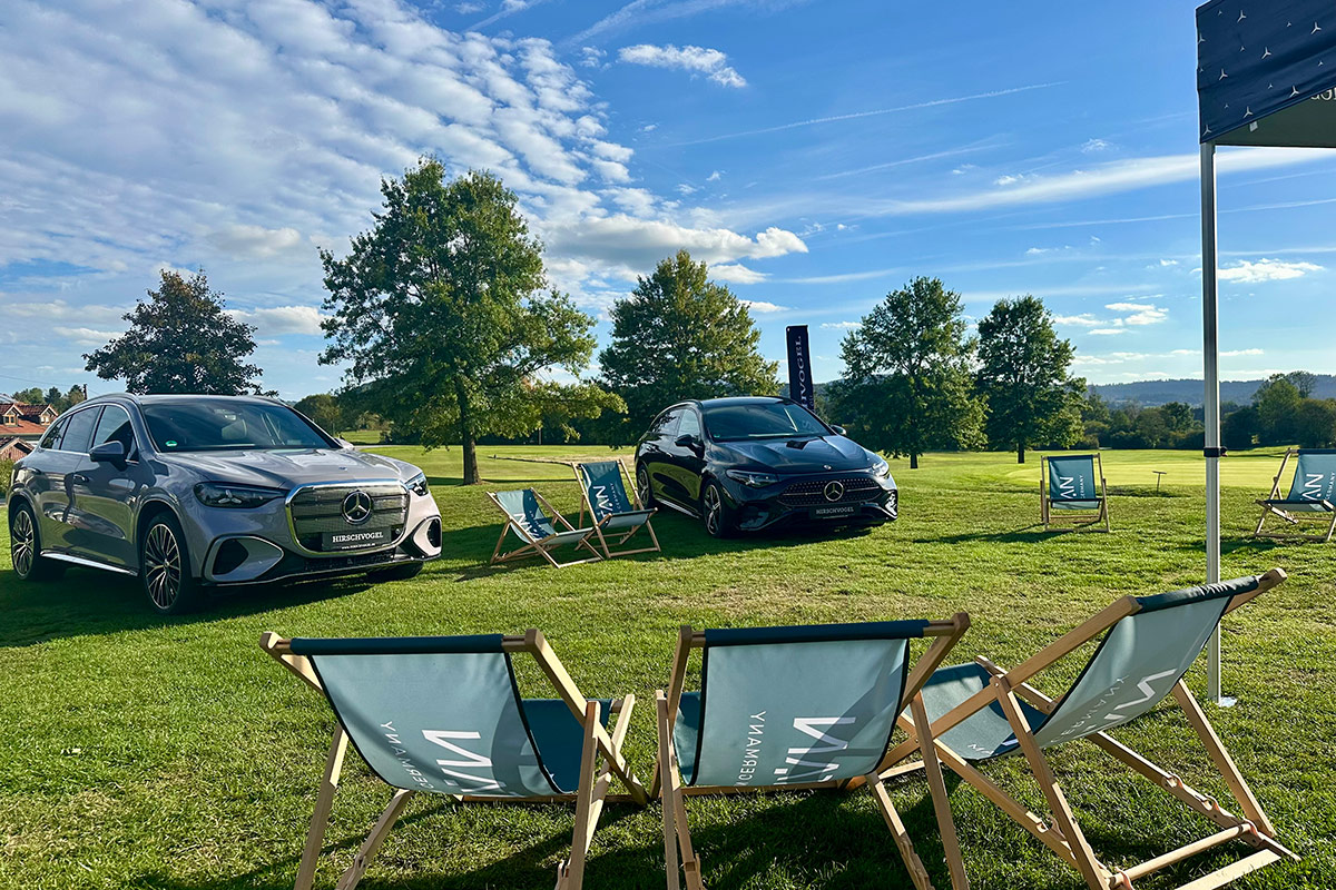 Auf einer großen, gepflegten Rasenfläche eines Golfplatzes sind zwei Mercedes-Benz Fahrzeuge ausgestellt. Links steht ein silberfarbenes SUV, rechts ein dunkles Kompaktfahrzeug. Vor den Fahrzeugen und auf der gesamten Fläche sind mehrere Liegestühle mit dem Schriftzug „TITAN“ aufgestellt.