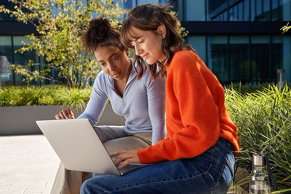 Zeigt zwei Personen, die sich auf einem Laptop etwas ansehen.