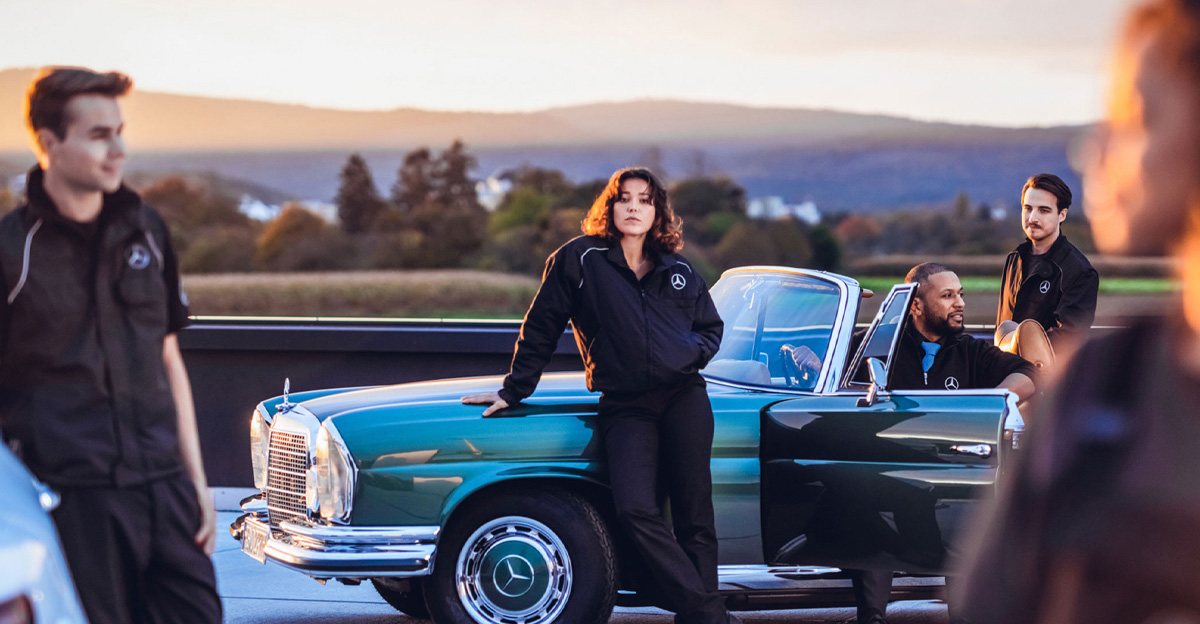 Gruppenszene mit einem klassischen Mercedes-Auto bei Sonnenuntergang.